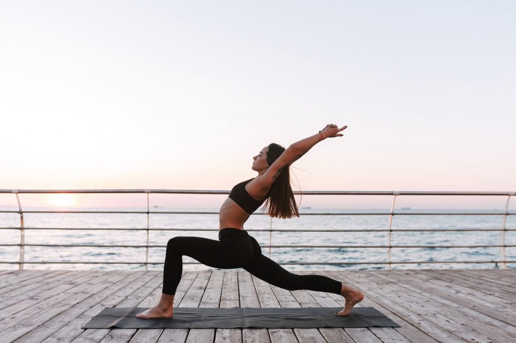 Beautiful young lady standing and training yoga poses by the sea